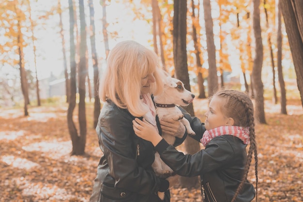 Oma met kleindochter in herfstpark, meisje knuffelen grootmoeder en haar jack russell terrier-hond. Generaties, huisdier en familie concept.