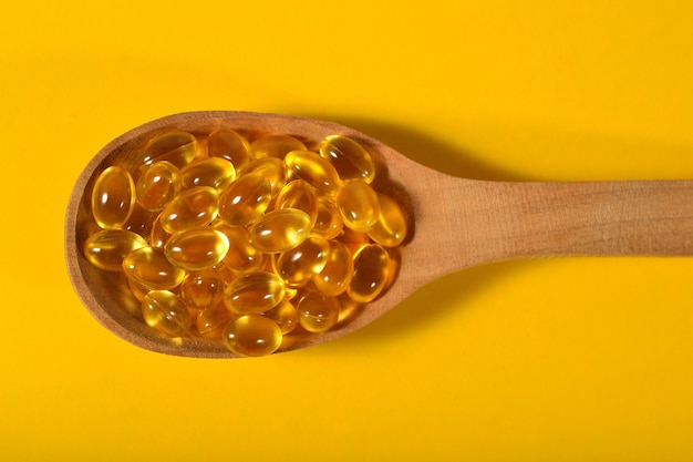 Omega-3 fish fat oil capsules in wooden spoon on a yellow background