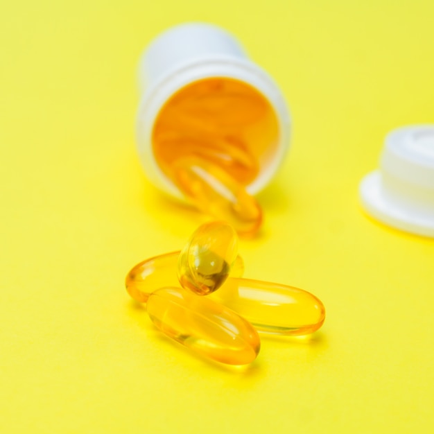 Omega 3 fish oil gel capsules on  yellow background. Creative health care concept