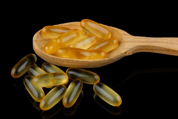 Omega 3 gelatin capsules in a wooden spoon on a black background