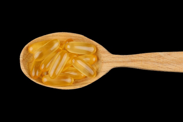 Omega 3 gelatin capsules in a wooden spoon on a black background