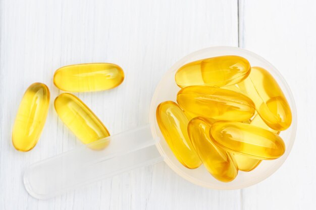 Omega-3 yellow capsules in a plastic scoop, nutritional supplements, close-up, top view.