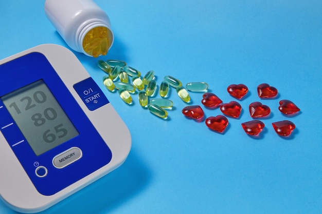 Photo omega3 polyunsaturated fatty acids and red decorative and cardiac tonometer on a blue background prevention and treatment of atherosclerosis hypertension and ischemic disease
