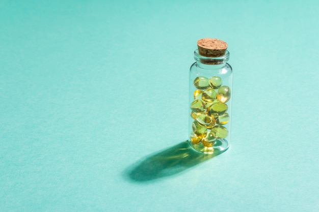 Omega3 tabletten in een oude fles op een turquoise mat.