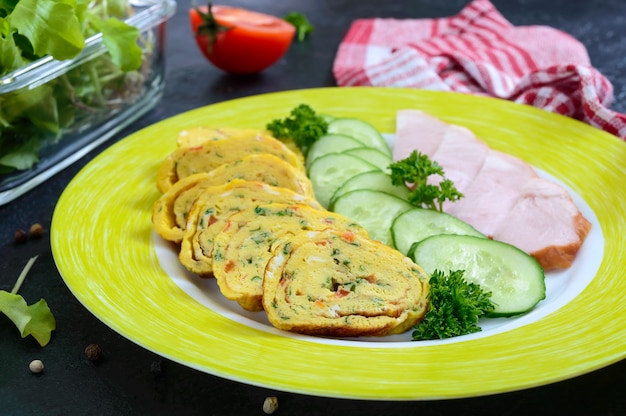 Omelet, loempia met ham en verse komkommer op een zwarte achtergrond.