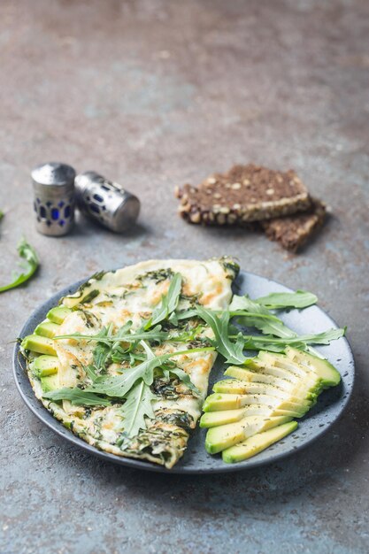 Omelet met avocado en rucola op grijze keramische plaat op stenen ondergrond, bovenaanzicht. Gezond ontbijt.