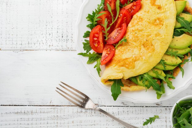 Omelet met avocado, tomaten en rucola op witte keramische plaat op lichte stenen achtergrond