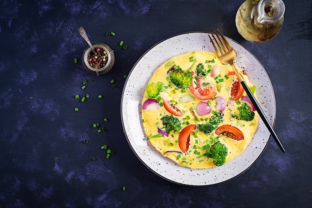 Omelet met broccoli, tomaten en rode uien op donkere tafel. Italiaanse frittata met groenten. Bovenaanzicht, boven het hoofd