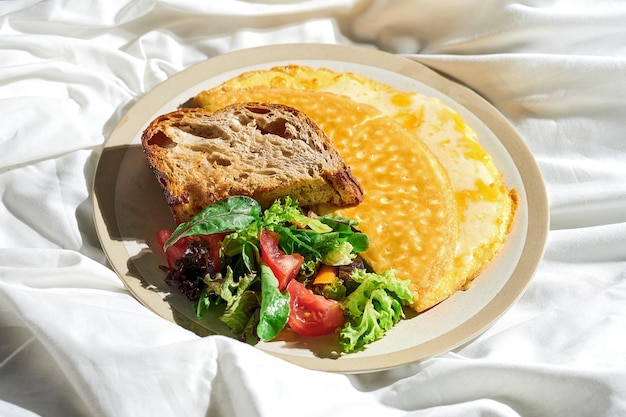 Omelet met gesmolten kaas groentesalade en toast in een bord op een wit laken Stoer licht