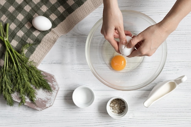 Omelet met kruiden koken, vrouwelijke handen breken een ei, recept stap voor stap, bovenaanzicht