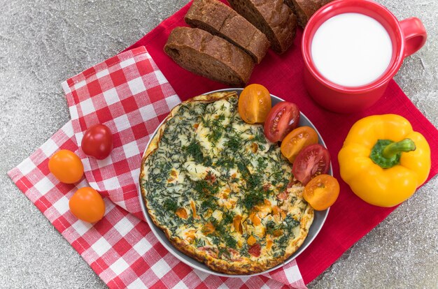Foto omelet met tomaat, kruiden, brood pepers en mok melk op linnen servet voor het ontbijt