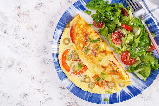 Omelet met tomaten, groene olijven en verse salade op blauw bord Frittata Italiaanse omelet