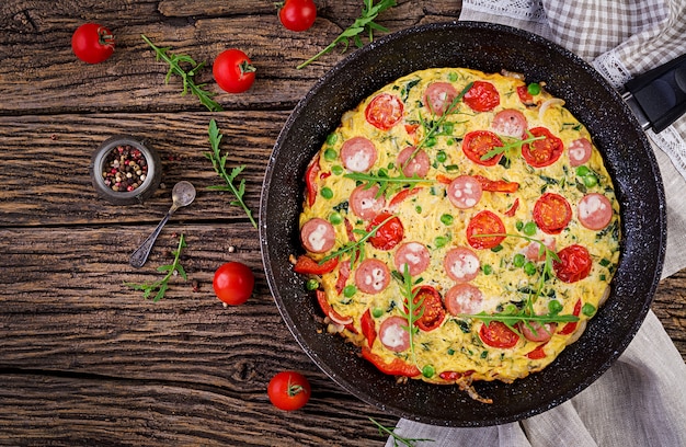 Omelet met tomaten, worst en groene erwten in rustieke stijl. Frittata - Italiaanse omelet. Bovenaanzicht