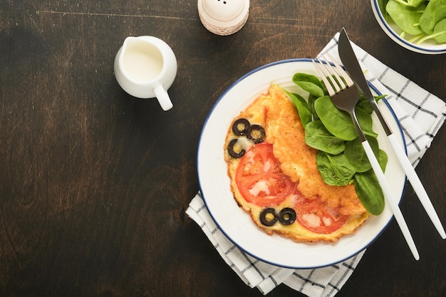 Omelet met tomaten zwarte olijven kwark en groene spinazie kruiden op witte plaat op oude houten rustieke donkere achtergrond heerlijk ontbijt gezond ontbijt eten bovenaanzicht