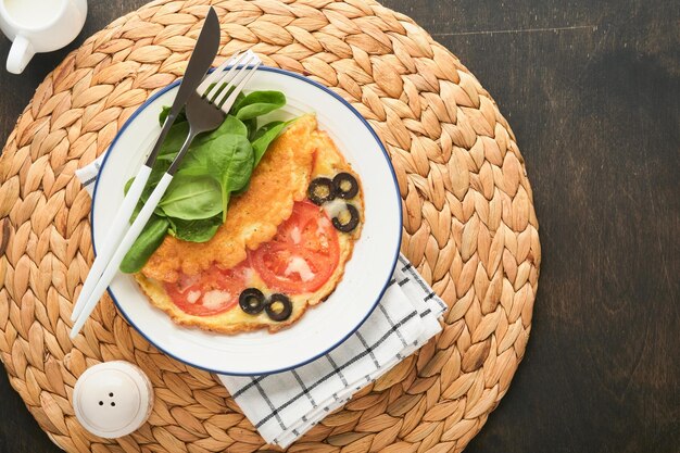 Omelet met tomaten zwarte olijven kwark en groene spinazie kruiden op witte plaat op oude houten rustieke donkere achtergrond heerlijk ontbijt gezond ontbijt eten bovenaanzicht
