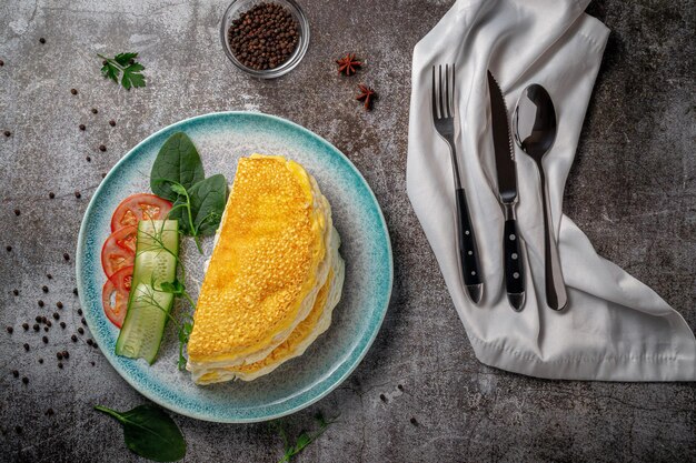 Omelet met verse kruiden en tomaten in een blauw bord met kruiden tegen een grijze stenen tafel