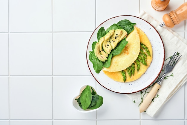 Omelet of met asperges, avocado en spinazieblaadjes op een betegeld oppervlak. Bovenaanzicht.