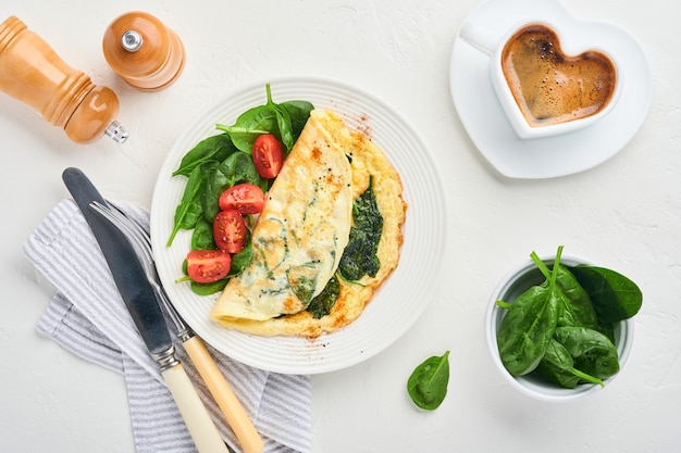 Omelet or omelette with spinach, cherry tomato and pepper seasoning on a white plate, on white background. Top view.