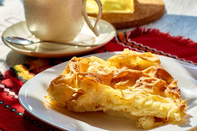 An omelet in a plate on a wooden table a teapot and a mug