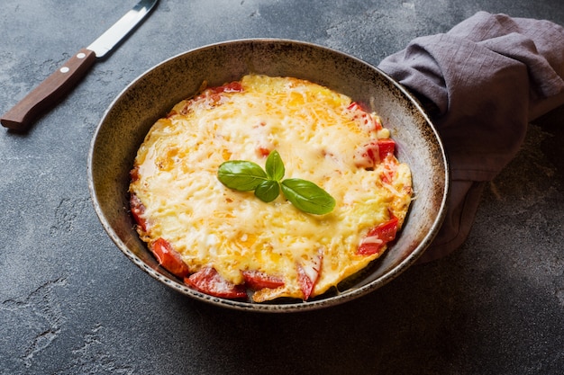 Omelet, roerei met tomaten en kaas in een pan op een donkere tafel.