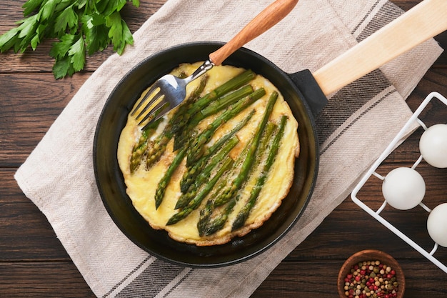Omelet with asparagus Frittata or scrambled with asparagus in frying pan with parsley and pepper on old wooden table background Useful breakfast concept Top view