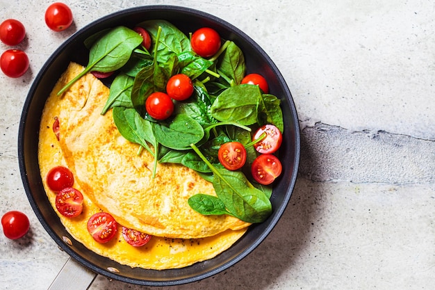 Omelet with fresh spinach and tomato salad in frying pan on gray table Breakfast food