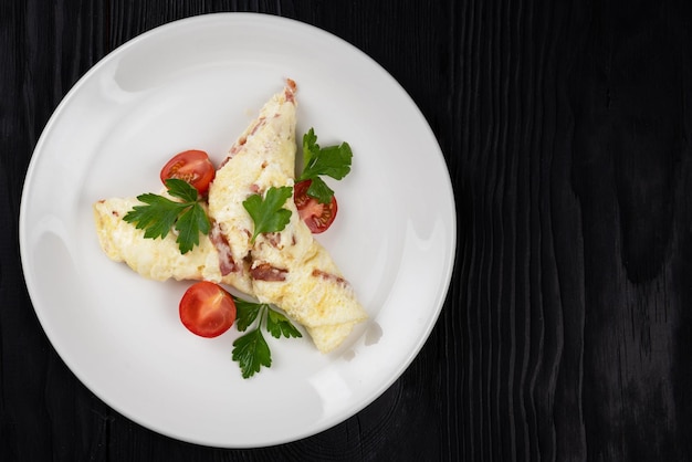 Omelet with ham and cheese and fresh vegetable on black wooden background
