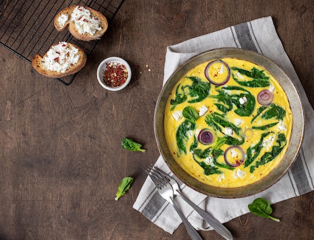 Omelet with spinach and feta cheese in an iron pan on a wooden, rustic . Top view. copyspace    