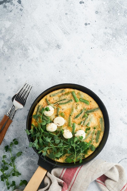 Omelet with spinach green beans potato and spinach healthy food in black frying pan on grey stone old rustic background Traditional frittata for breakfast Eggs tortilla Top view flat lay Copy space