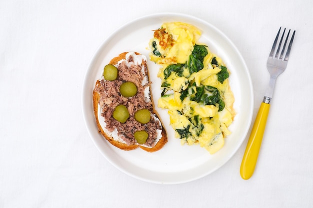 Foto omelette con foglie di spinaci con panino di tonno e formaggio a crema e omelette di cetriolo salato sul piatto