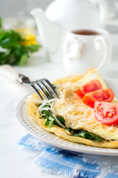 明るい背景の朝食にほうれん草、パセリ、チーズのオムレツ。