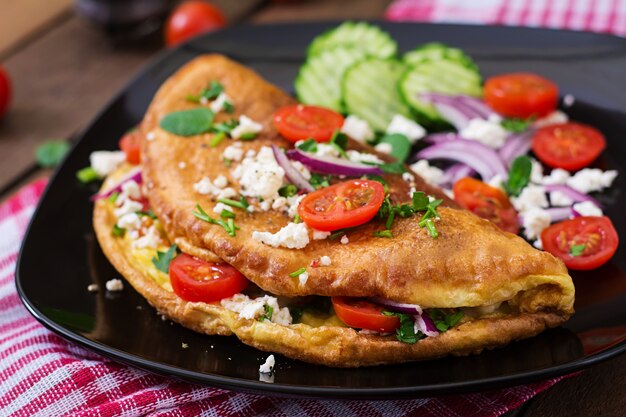 Omelet with tomatoes, parsley and feta cheese on black plate.