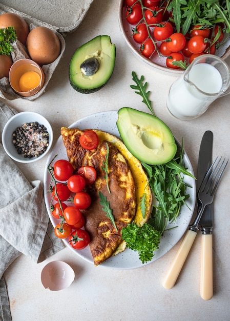 Omelette served with avocado cherry tomatoes and arugula Healthy and tasty keto breakfast or brunch