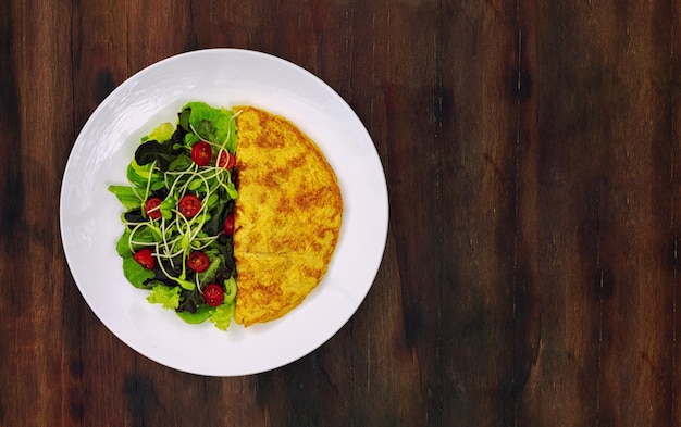 Foto omelette e insalata di verdure in un piatto di ceramica bianca posto sul tavolo di legno