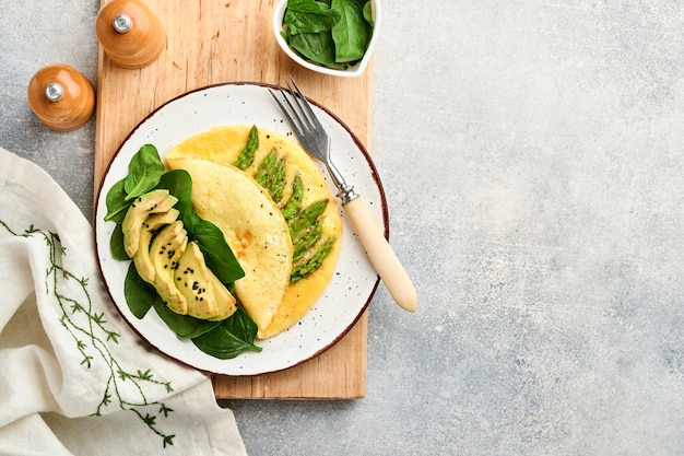 Omelette or with asparagus, avocado and spinach leaves on concrete surface. Top view.