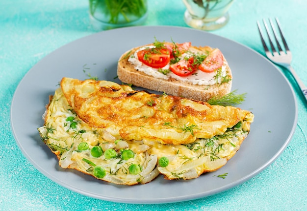 Omelette with green peas onions and toast cream cheese tomatoes on blue plate Frittata italian omelet