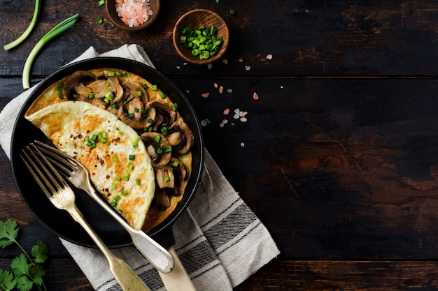 Omelette with mushrooms and green young onions on cast iron pan on old wooden surface.