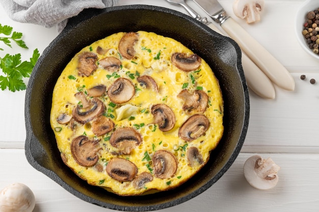 Omelette with mushrooms and herbs in a pan on a white wooden background Healthy breakfast Top view