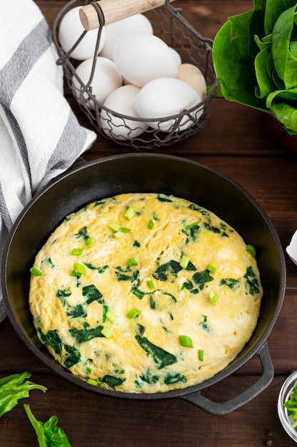 omelette with spinach, green onions and feta cheese in a cast-iron frying pan . 