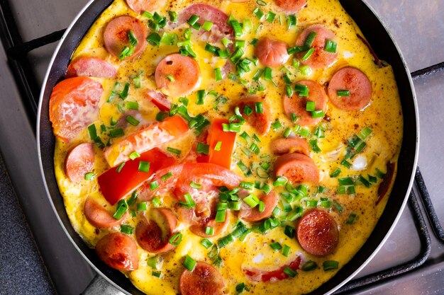 Omelette with tomato, onion and sausage on frying pan