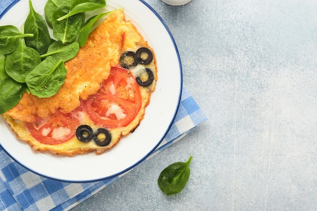 Omelette with tomatoes black olives cottage cheese and green\
spinach herbs on white plate on grey concrete background delicious\
breakfast healthy breakfast food top view