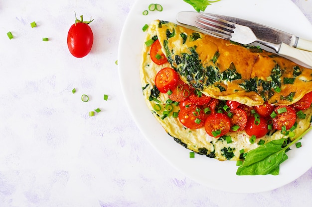 Omelette with tomatoes, spinach and green onion on white plate.