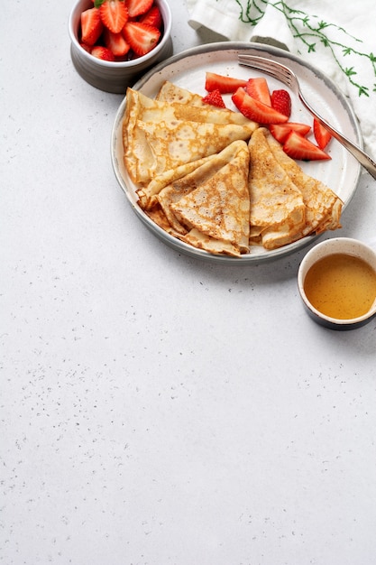 Omfloerst pannekoeken met verse aardbei op witte ceramische plaat. Bovenaanzicht.