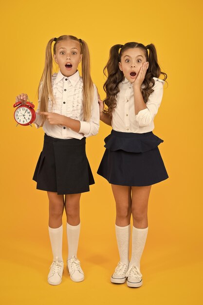 OMG Got a surprise Surprised schoolgirls checking time on yellow background Shocked little children having mouth open with surprise being late Back to school surprise Surprise concept