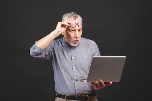 OMG! I'm shocked! Scared senior aged bearded old man in eyeglasses holding laptop computer