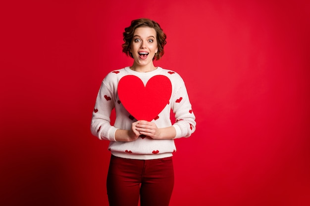 Omg is het voor mij? Portret van gek vrolijk positief meisje houdt groot papieren kaarthart ze krijgt op 14-februari-viering broek dragen trendy broek geïsoleerd over levendige kleurenmuur