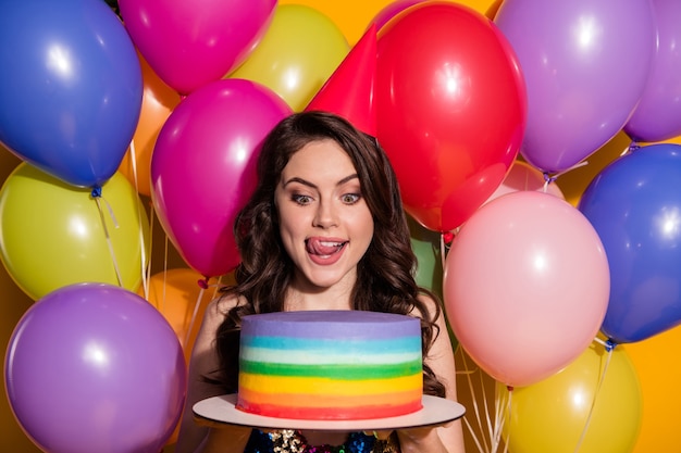 Omg lets eat whole cake. Positive excited girl celebrate anniversary event hold birthday pastry look lick lips wear dress sequins isolated with balloons bright shine color background