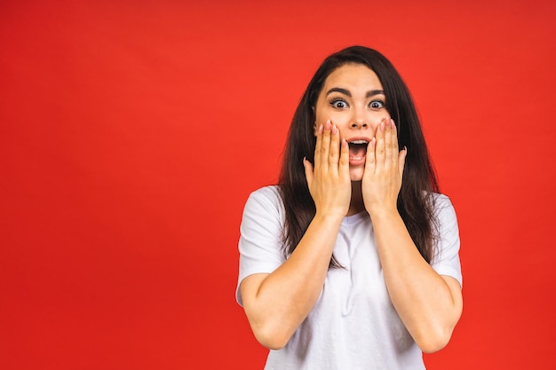 OMG Portrait of amazed shocked surprised young woman isolated over red background