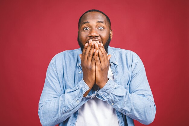 Omg. Portrait of funny young black man with mouth wide opened and jaw dropped, his whole look expressing shock isolated over red.