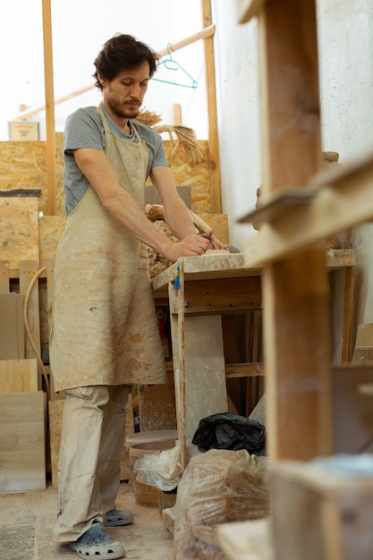 Omgaan met klei. hardwerkende sterke man met donkere baard die in een uitgeruste pottenbakkerij verblijft en nieuw materiaal verwerkt